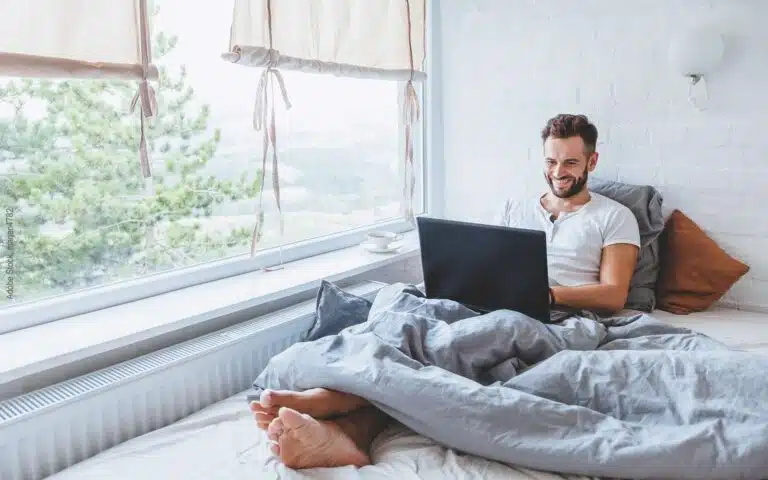 un homme surfe allongé sur son lit avec un PC