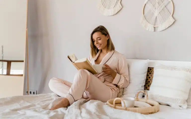 une femme prend son café en lisant sur son matelas