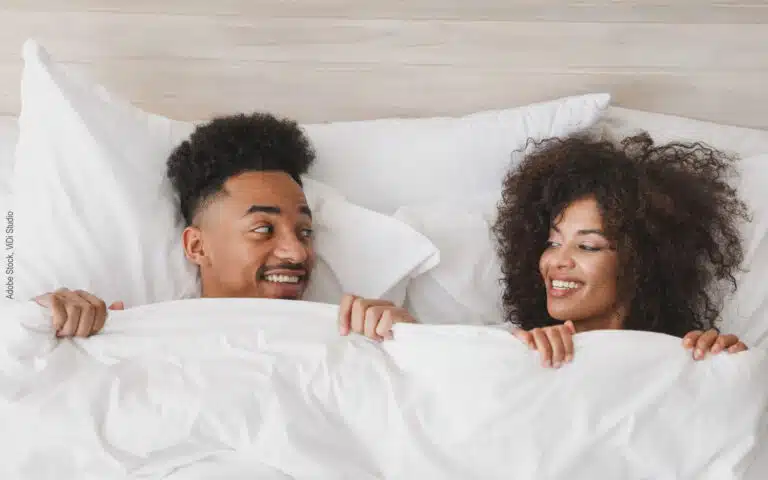 une jeune couple se sourit sous la couette