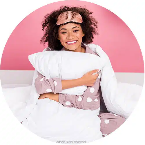 jeune femme sur fond rose avec un masque de sommeil et un oreiller