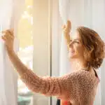 une femme ouvre les rideaux pour aérer sa chambre
