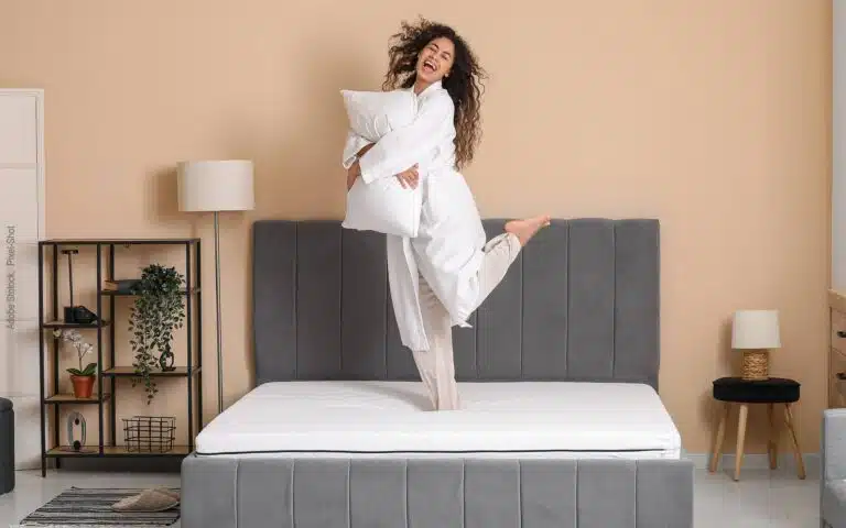 une jeune femme danse sur son lit avec un oreiller