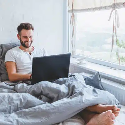 un homme fait ses achats en ligne sur son lit