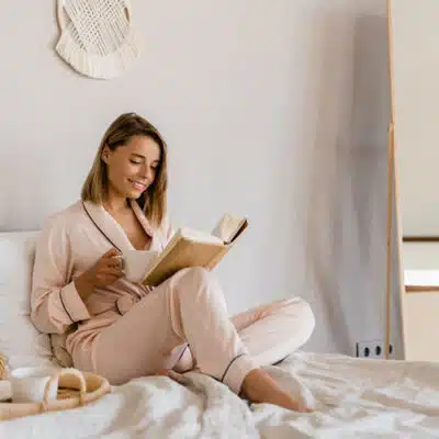 une femme lit sur son lit en prenant son café