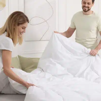 une femme aidée par son mari pose la couette sur le lit