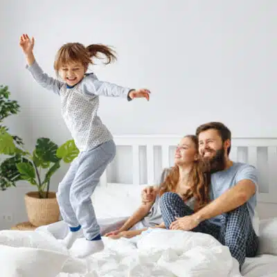 une petite fille danse sur le lit devant ses parents