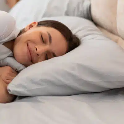 une femme sourit en serrant son oreiller dans son lit