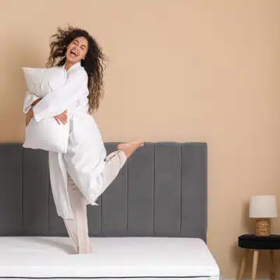 une femme tient un oreiller et danse sur son lit