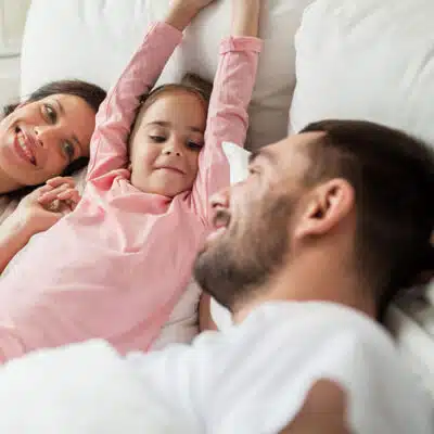 une petite fille s'étend entourée de son papa et sa maman
