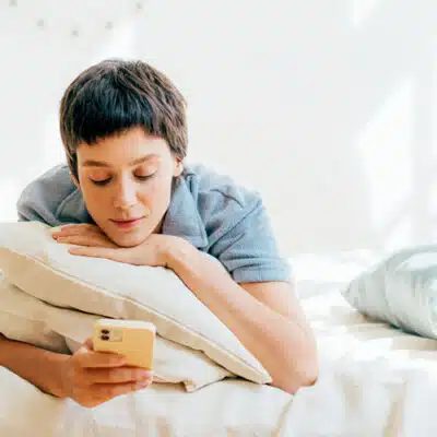 une femme s'appuie sur ses 2 oreillers pour consulter son smartphone