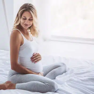 une femme enceinte les mains sur le ventre sur son lit