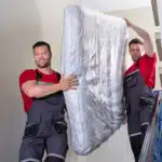 Deux livreurs portent un matelas dans un escalier