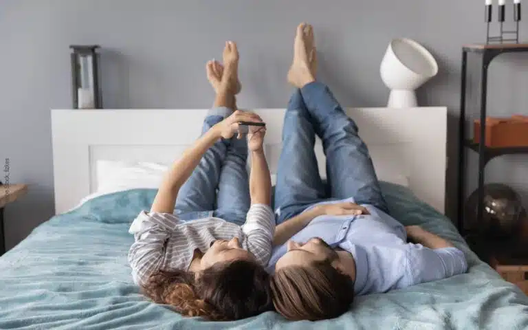un couple allongé sur son lit les pieds en l'air en train de regarder un iPhone