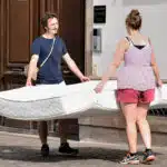 un jeune couple porte un matelas usagé vers la déchetterie