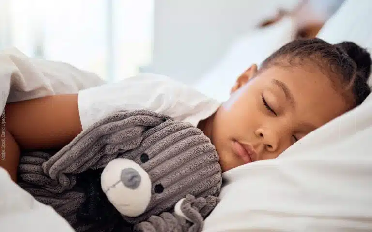 une petite fille dort paisiblement avec son ours en peluche
