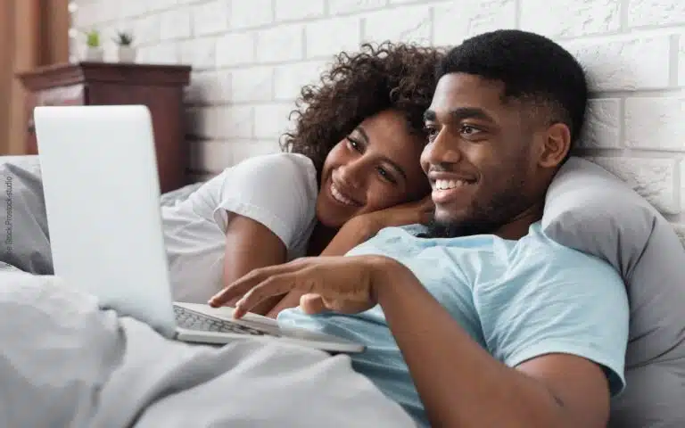 un jeune couple au lit qui regarde un PC